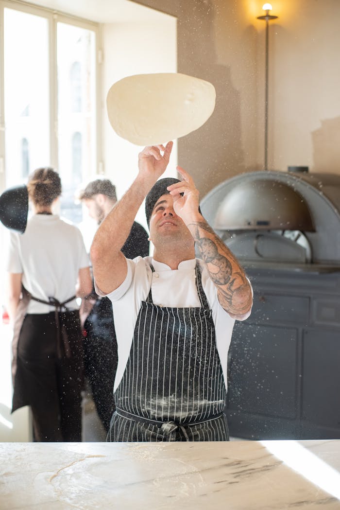 A chef in a traditional Portuguese bakery tosses pizza dough with skill, illuminated by natural daylight.